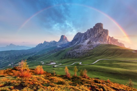 Mountain landscape scene in the alps with winding road and rainbow