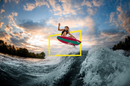 Woman jumping over big splashing wave on surf style wakeboard