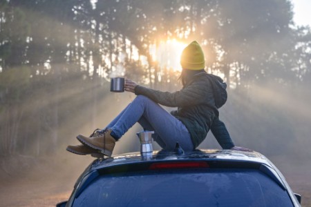 Woman traveller enjoying coffee time on roof of the car