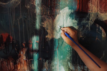 Mão do artista segurando a pintura de pincel em uma tela