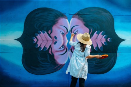 
            Umelkyňa maľujúca na exteriérovú stenu v mestskom verejnom parku
        
