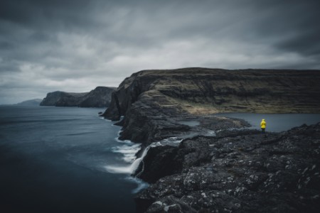 Person in yellow coat against mountains faroe islands