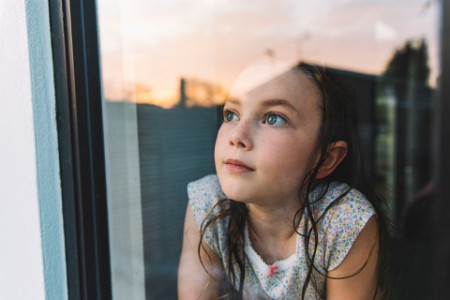 Young girl looking through window at sunset image