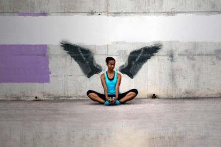 Jovem mulher em frente a um muro de concreto com desenho de asas
