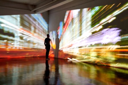 Man looking into a nighttime cityscape being projected in gallery space