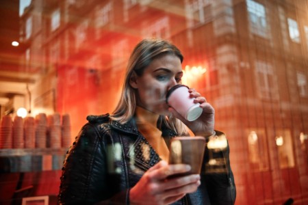 Vrouw met kop koffie en smart phone in cafetaria