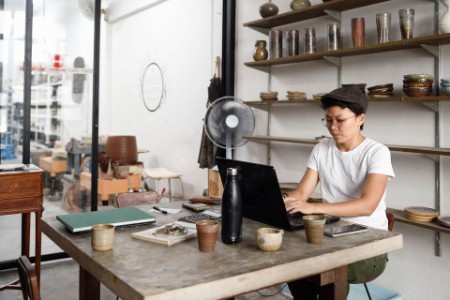 
            Jeune entrepreneure asiatique travaillant à l’ordinateur dans sa boutique
        