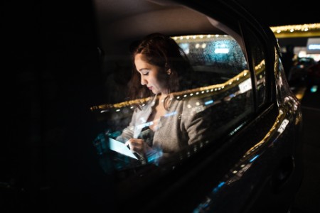 Jonge onderneemster die aan haar digitale tablet op de achterzetel van auto werkt