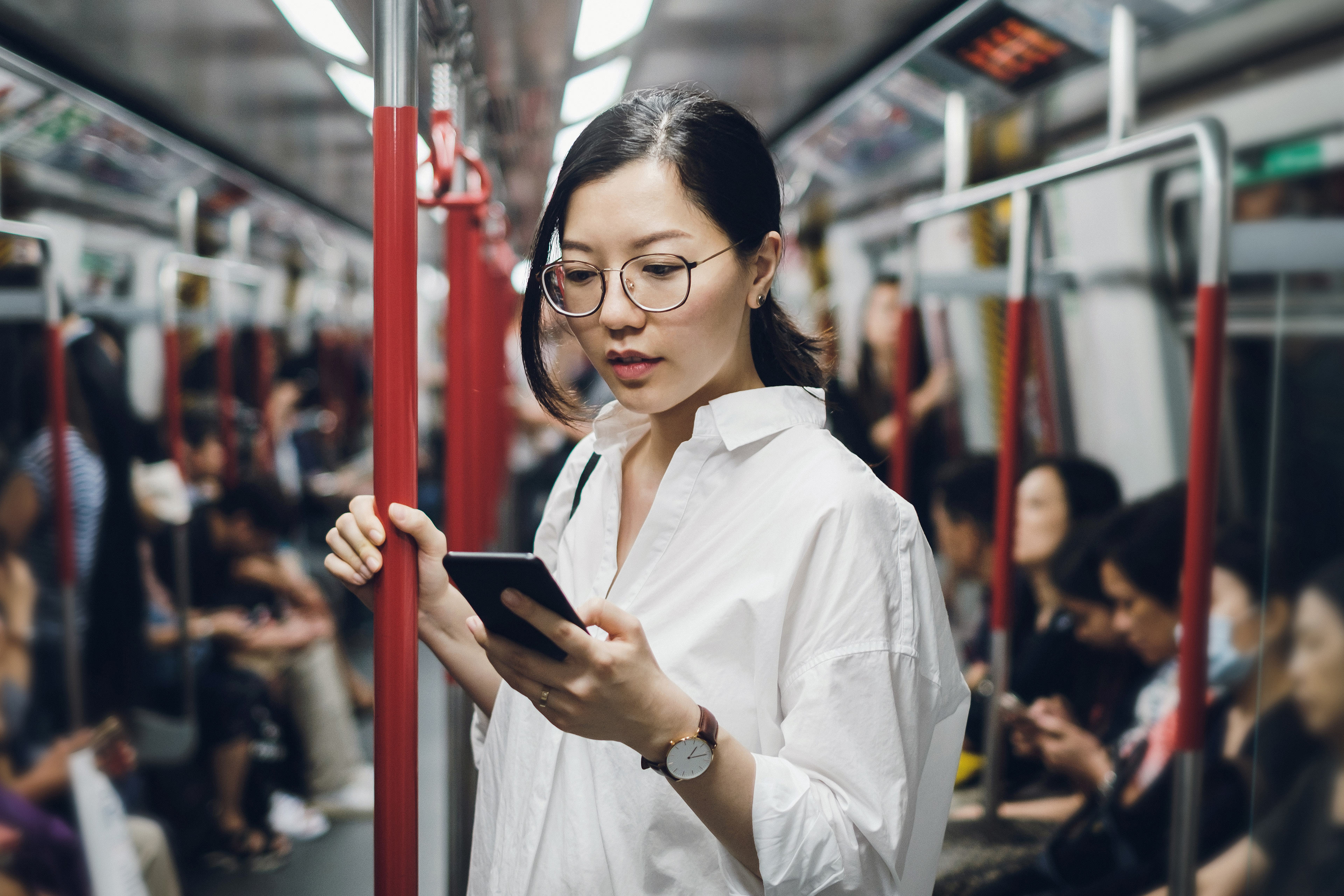 Une femme portant des lunettes consulte son cellulaire dans le métro.