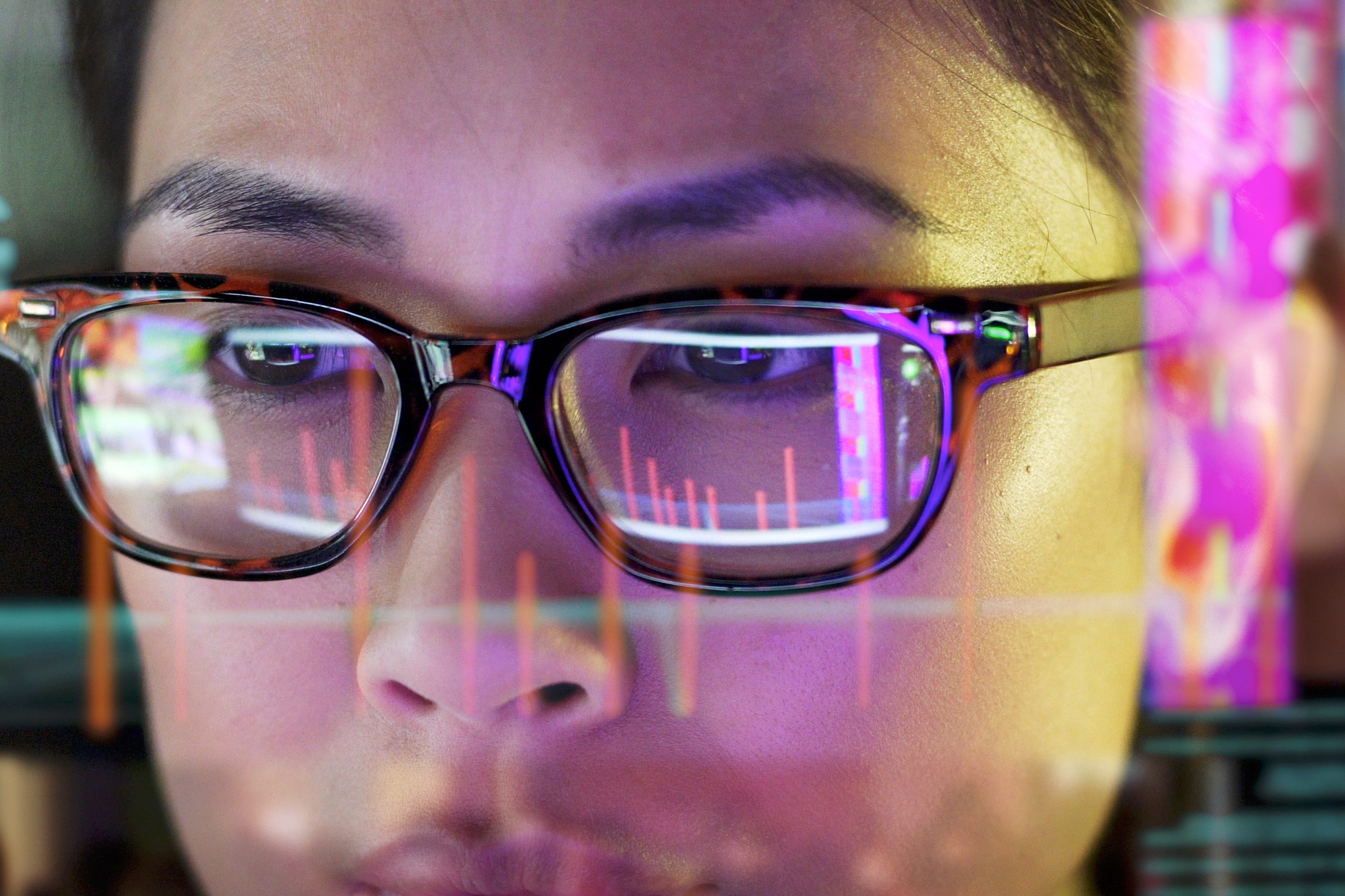 Tietokoneiden valot heijastuvat naisen silmälaseihin