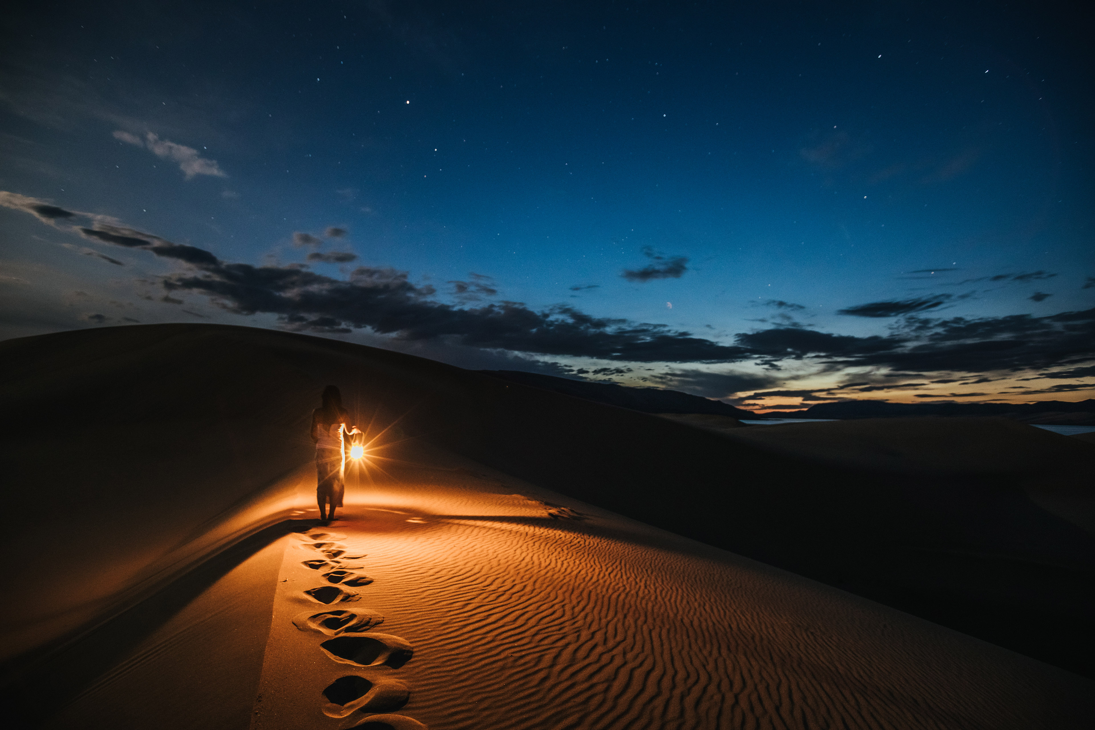 Muotokuva lyhtyä kantavasta naisesta, joka kävelee hiekkadyyneillä yöllä        