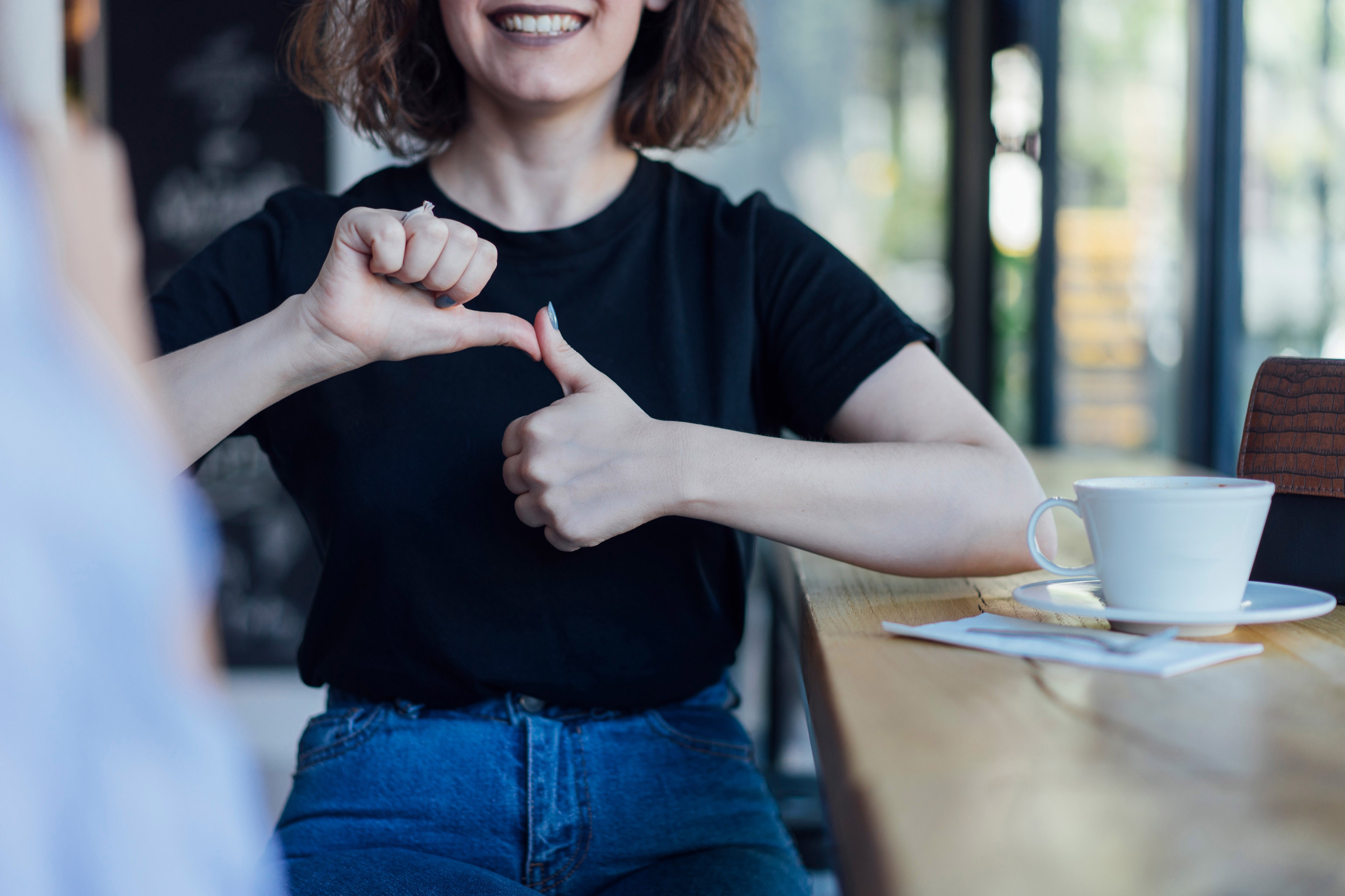Dvi moterys, kavinėje, bendrauja gestų kalba