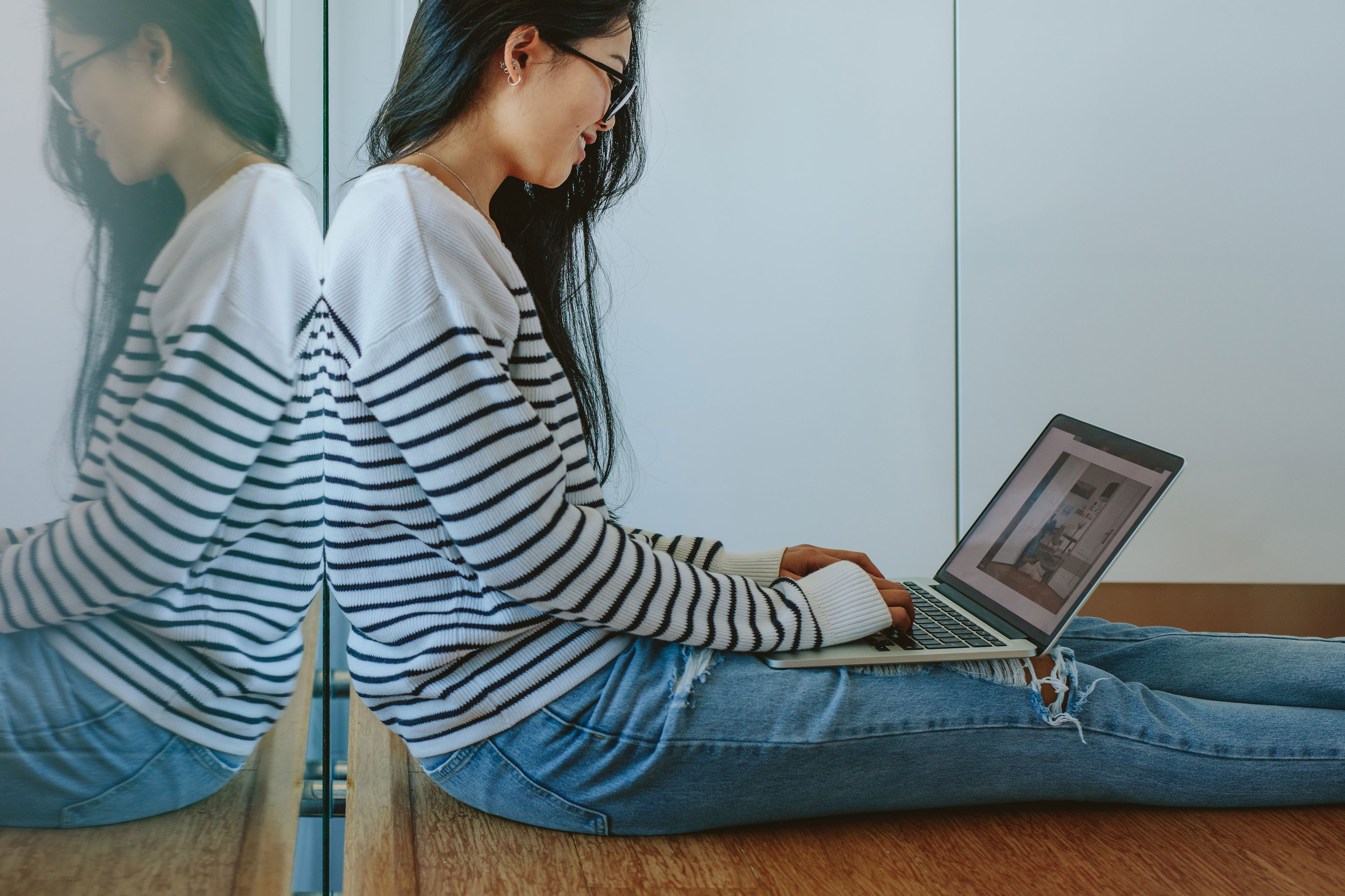 Jauna moteris su dryžuota palaidine sėdi su nešiojamu kompiuteriu ant
grindų