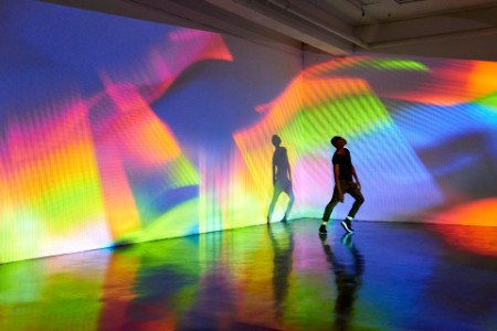 Homem dançando em frente a uma imagem projetada colorida em grande escala