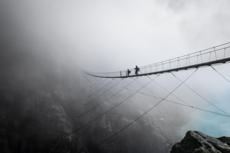 Two people cross suspension bridge by waterfall