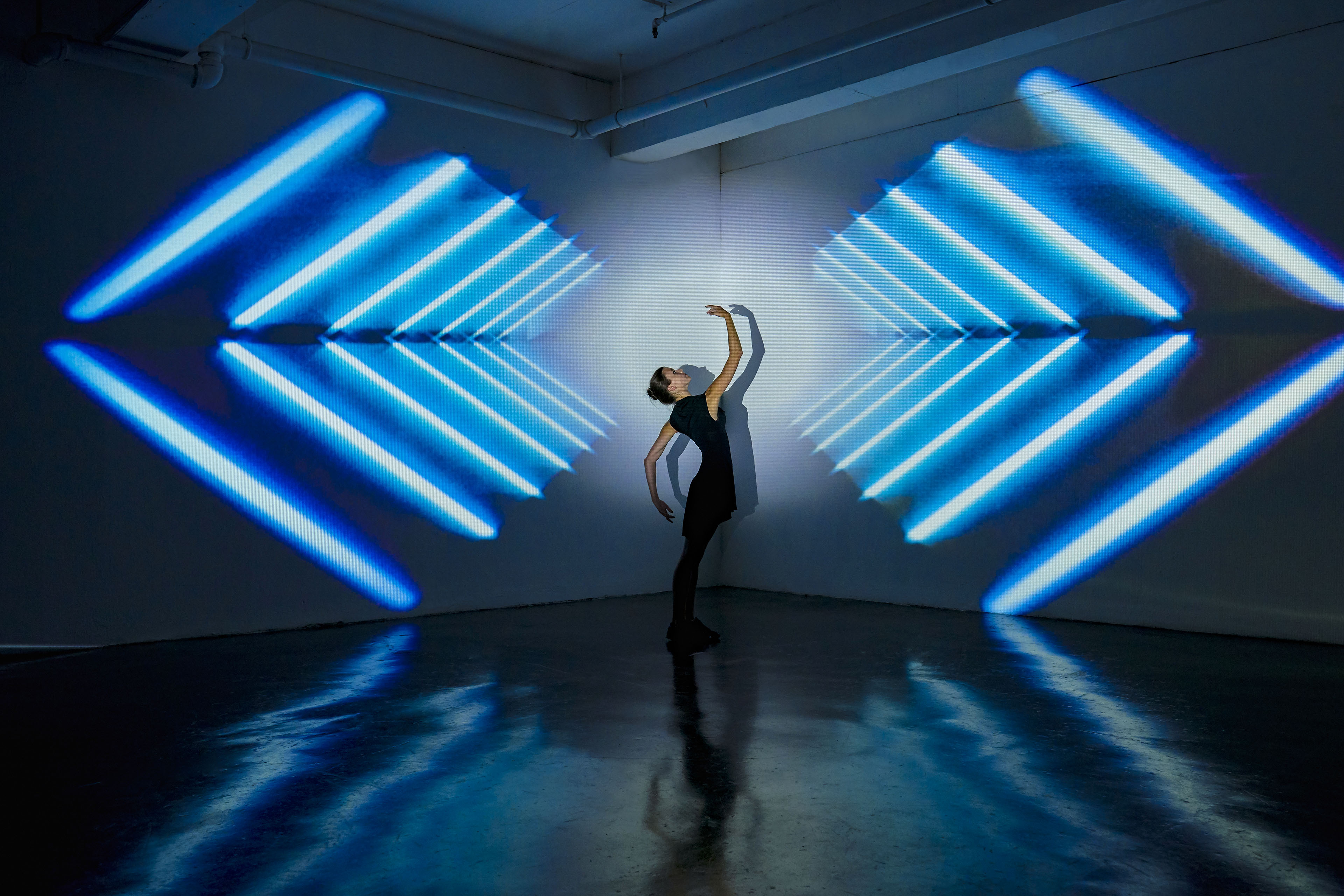 Girl dancing in a studio with graphic patterns projected onto wall behind her