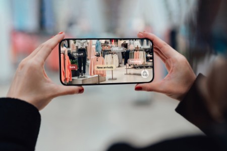 Mano sosteniendo un smartphone usando una aplicación de realidad aumentada para comprobar las ventas en una tienda de moda