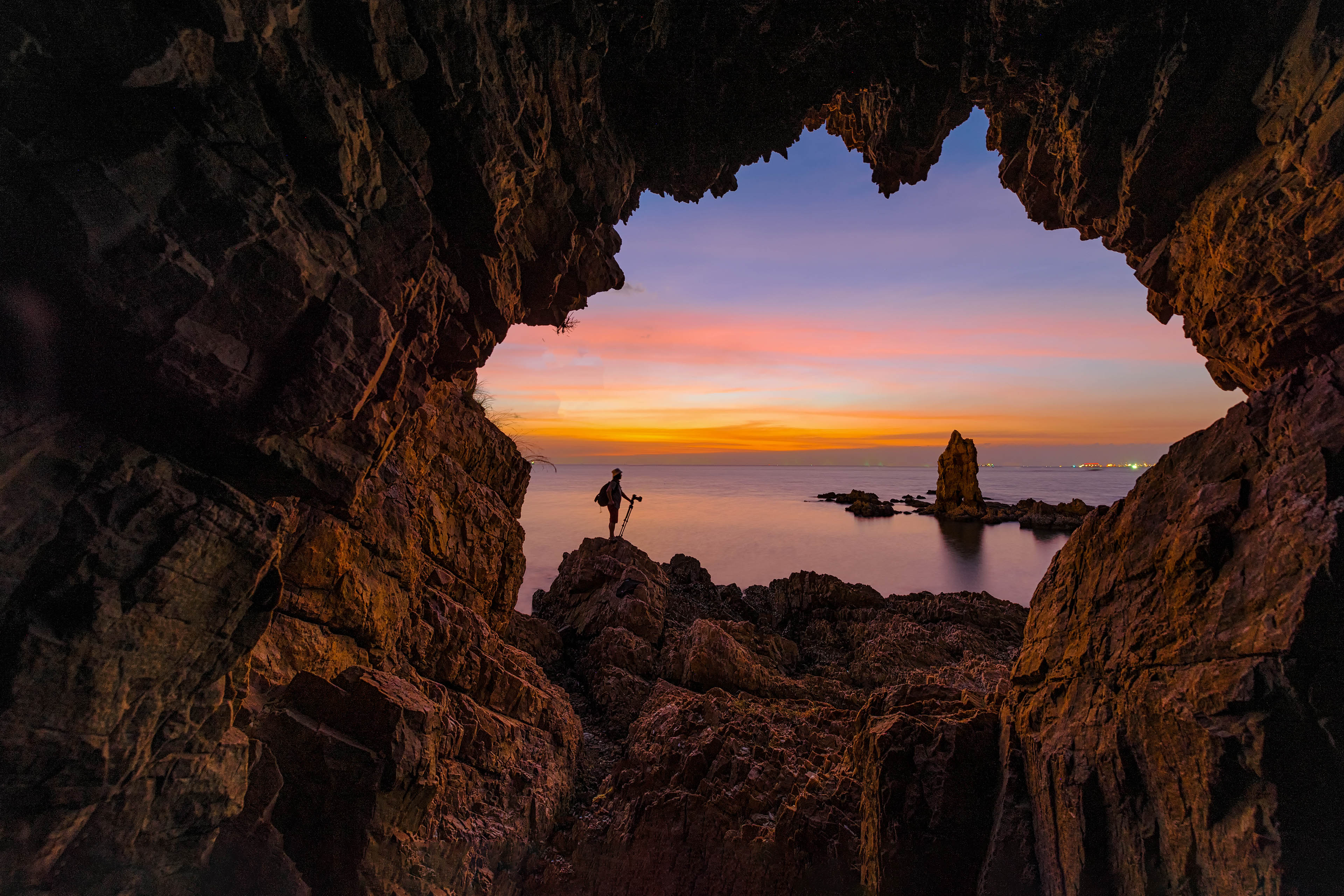Photographer stands in rock arch at sunset