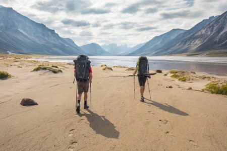 Rear view of two hikers walking along river bank