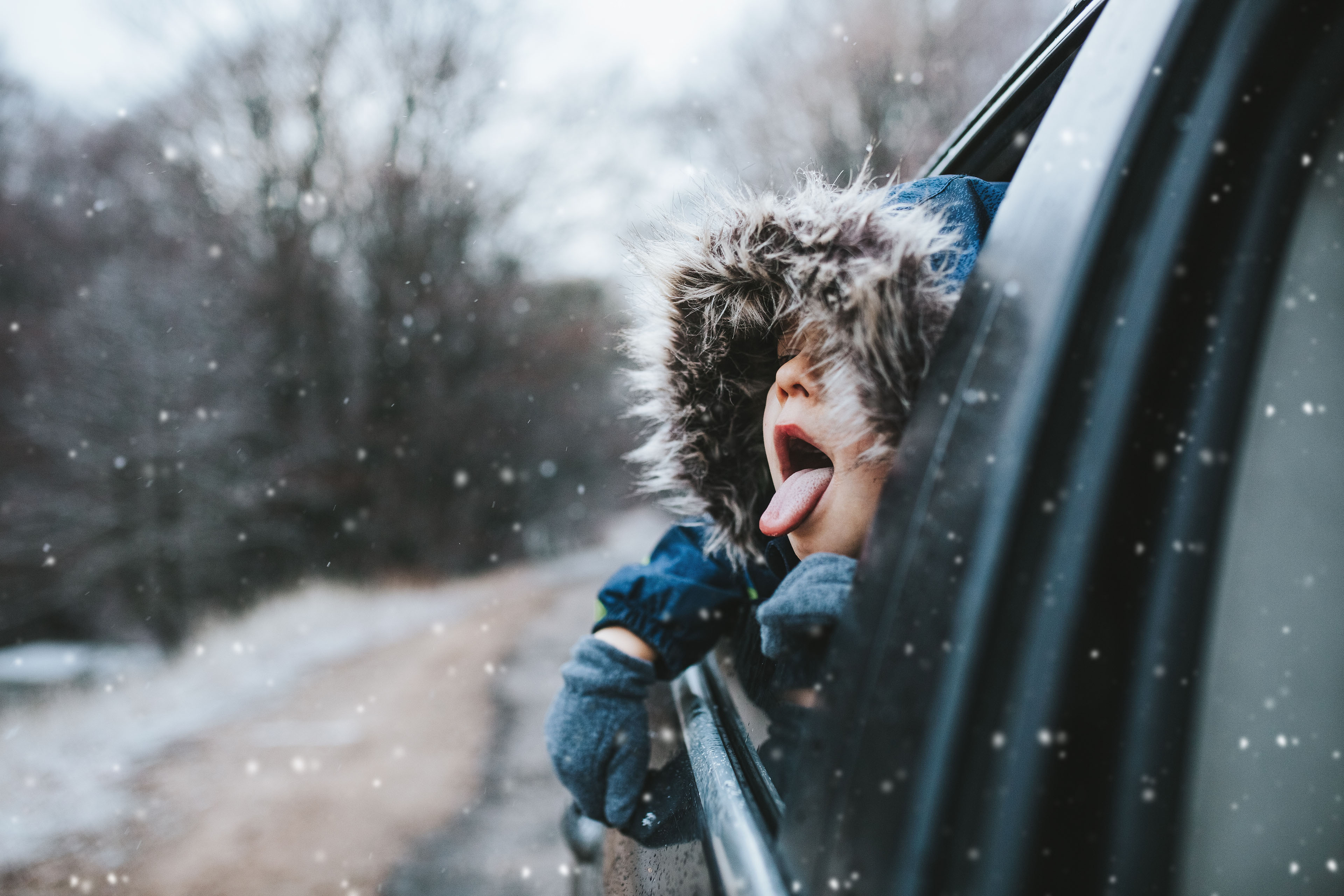 Boy catching snowflakes out of car window