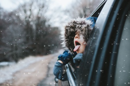 車の窓から顔を出し、雪を口でキャッチしようとする男の子