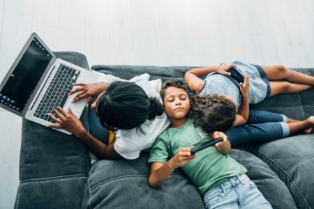 一個多元種族家庭坐在沙發上使用數位裝置的照片。
