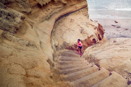 A photograph of a teenage girl running up steps by a beach.
