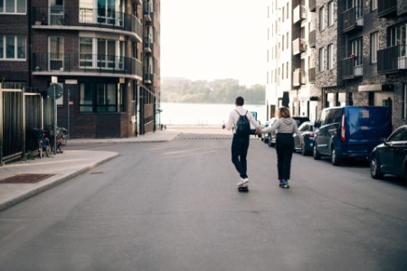 Photograph of two people holding hands while skateboarding down an empty street
