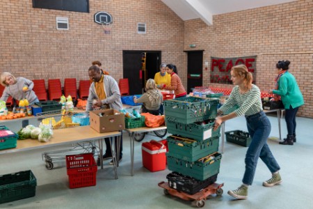 Fotografia dobrovoľníkov, ktorí v potravinovej banke organizujú zbierku potravín a ukladajú ich na stoly