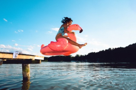 A photograph of a woman jumping into a lake while sitting on an inflatable pink flamingo floater