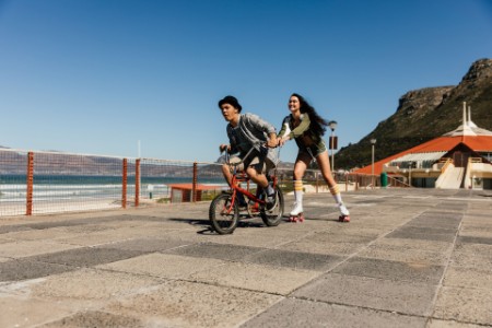 A photograph of a young man on a bicycle towing a girl on roller skates