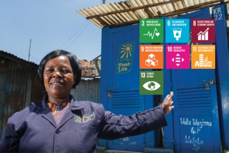 A woman poses by two sanergy toilet units