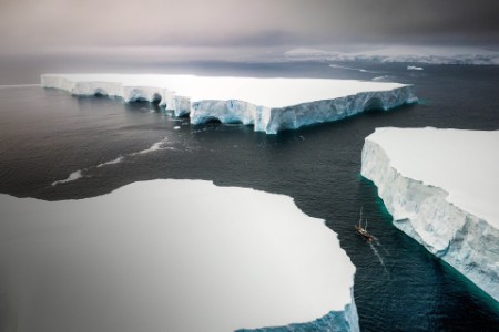 Ein Segelboot steuert durch riesige Eisberge hindurch