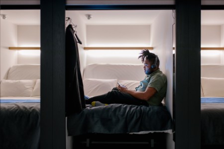 Man listening to music and using his smartphone in a capsule hotel