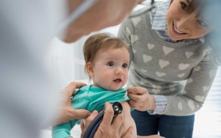 Doctor putting stethoscope on baby during checkup 