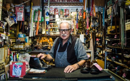 Señor mayor en un desordenado taller de reparación de zapatos