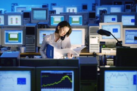 Woman working on telephone with report in hand, surrounded by computers