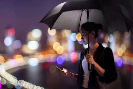 Businesswoman using mobile phone holding umbrella