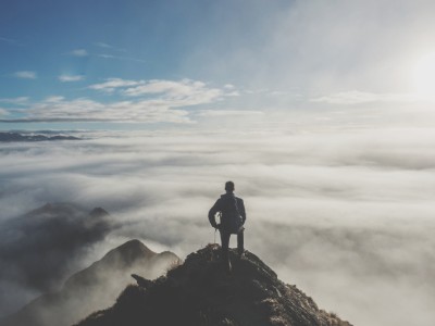 Hombre en la cima de una montaña mirando el horizonte cubierto por nubes