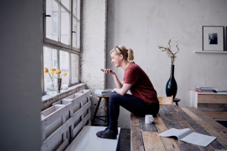 Woman sitting on desk in loft using cell phone