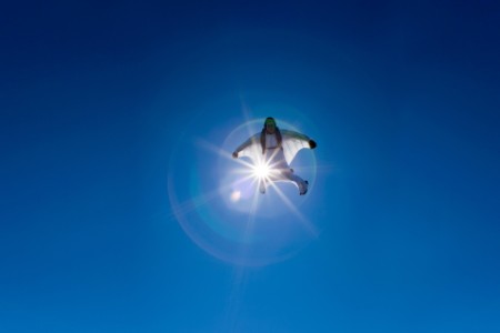 aerial view of flying white wingsuit with sunflare