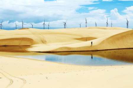 Man on sand dunes with wind turbines in background
