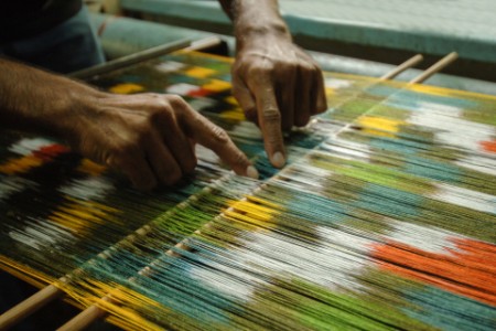 
            Manos de hombre detrás de un telar tejiendo una alfombra
        