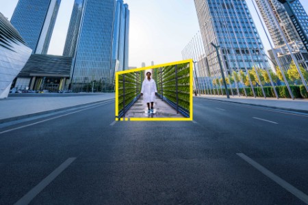 Woman in lab coat walks through a garden inside a yellow frame in the middle of an empty city road