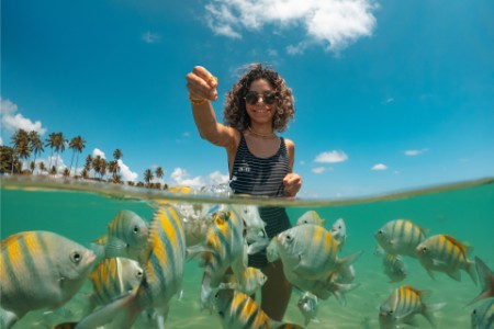 Young woman feeding fish on tropical beach