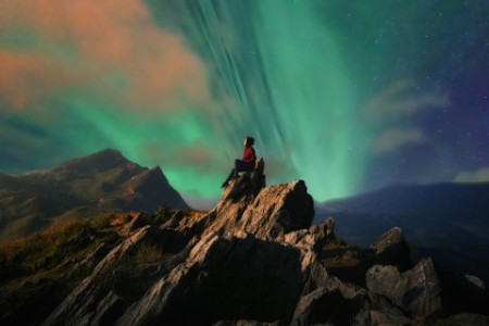 Mujer sentada en una roca mira una aurora boreal