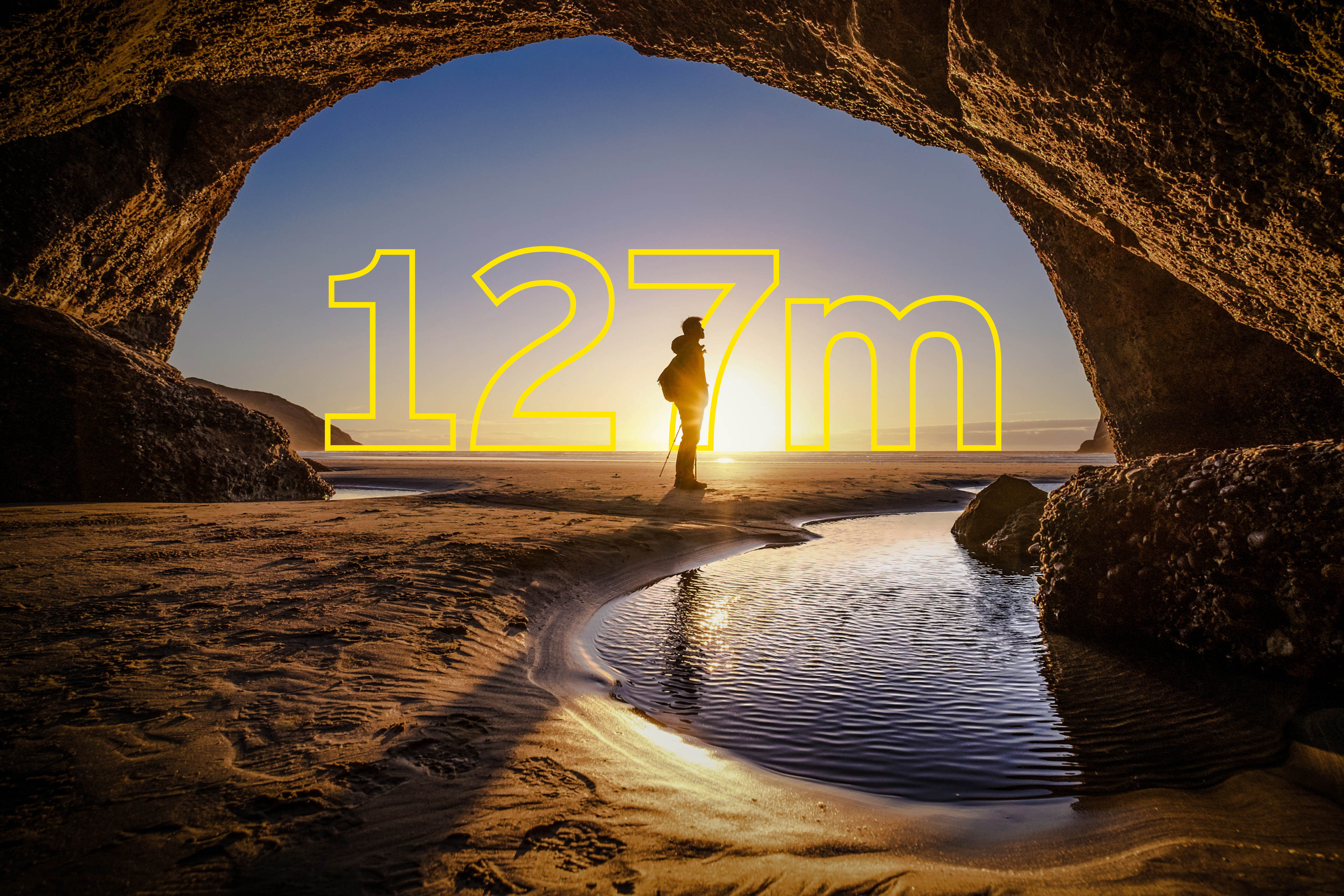 Young man stands at a cave exit in New Zealand - overlaid is yellow text saying 127m