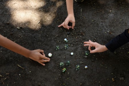 Three boys playing marbles in the dirt