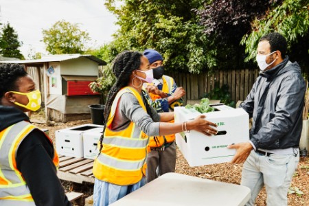 Man receiving csa box from volunteer at community garden