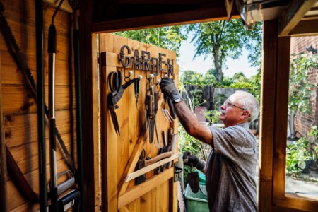 Senior man selecting hand tool from door of gardening shed